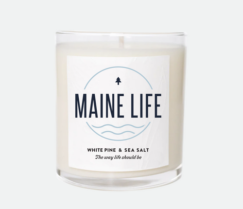 Candle that has Maine life logo on the front with a white pine and sea salt scent that reads 'The way life should be'